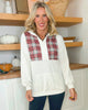 Woman wearing a white hoodie with plaid accents in a home setting with wooden shelves and pumpkins.