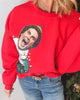 Red sweatshirt with a graphic design of a person in a festive outfit, worn by a person.