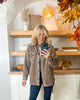 Woman taking a selfie in a beige jacket with autumn decorations in the background