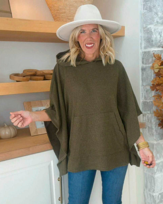 Woman wearing a green poncho and white hat indoors