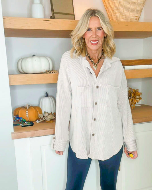 Woman wearing a beige shirt and blue jeans standing in a room with wooden shelves and pumpkins.
