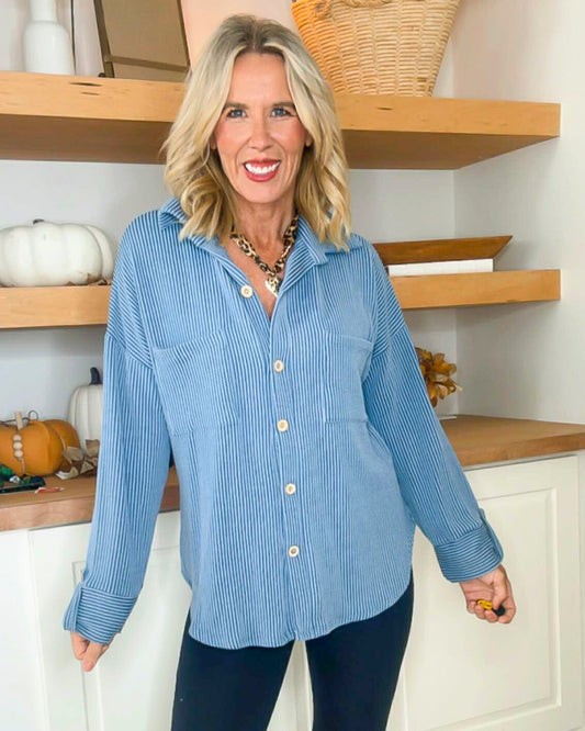 Woman wearing a blue striped shirt in a kitchen setting with wooden shelves and pumpkins.