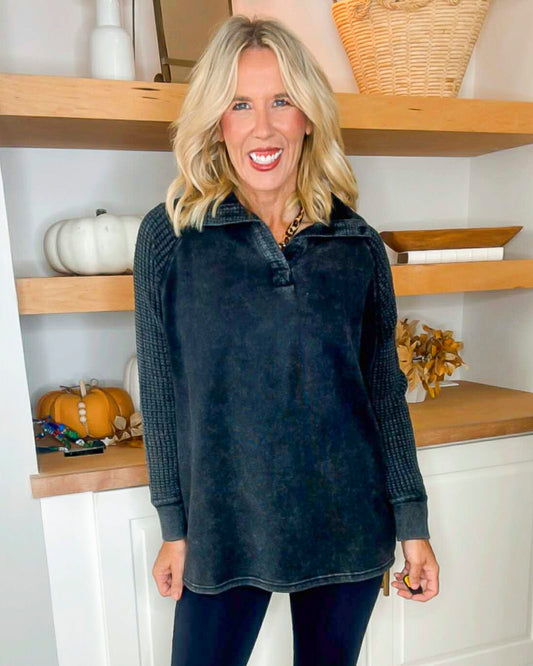 Woman wearing a dark blue pullover in a kitchen setting with wooden shelves and pumpkins.