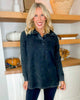 Woman wearing a dark blue pullover in a kitchen setting with wooden shelves and pumpkins.