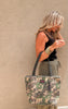 Close-up of camo tote bag with black handles and tassel charm, part of the Makeup Junkie collab collection.