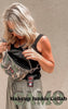 Woman holding a camo print crossbody sidekick bag by Makeup Junkie & Bad Habit, styled with a black tank and olive pants.