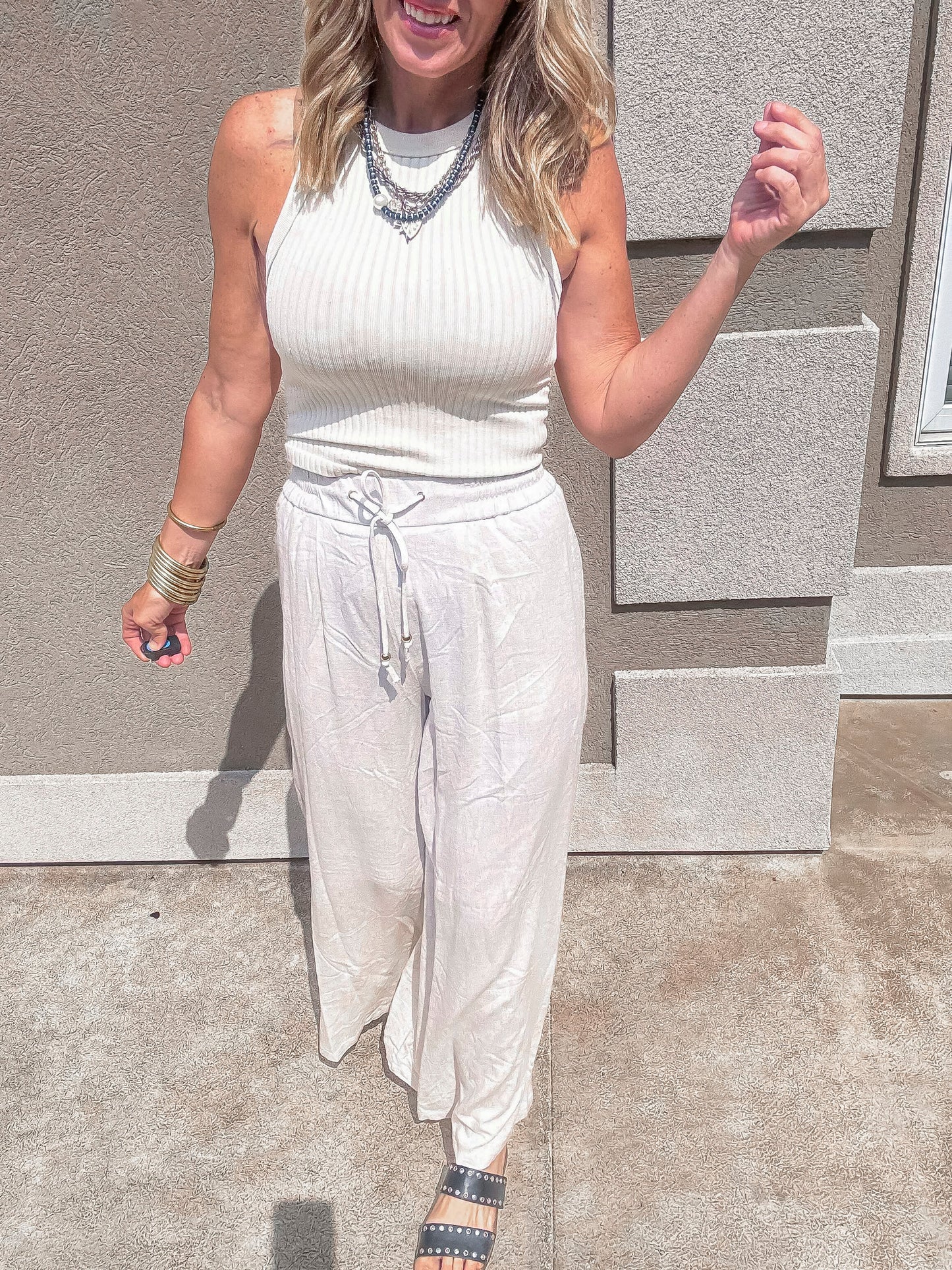 Flowy and lightweight khaki palazzo pants shown in motion, styled with neutral tones and studded slides for effortless style.