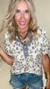 Woman wearing a leopard print top and denim shorts with a neutral background